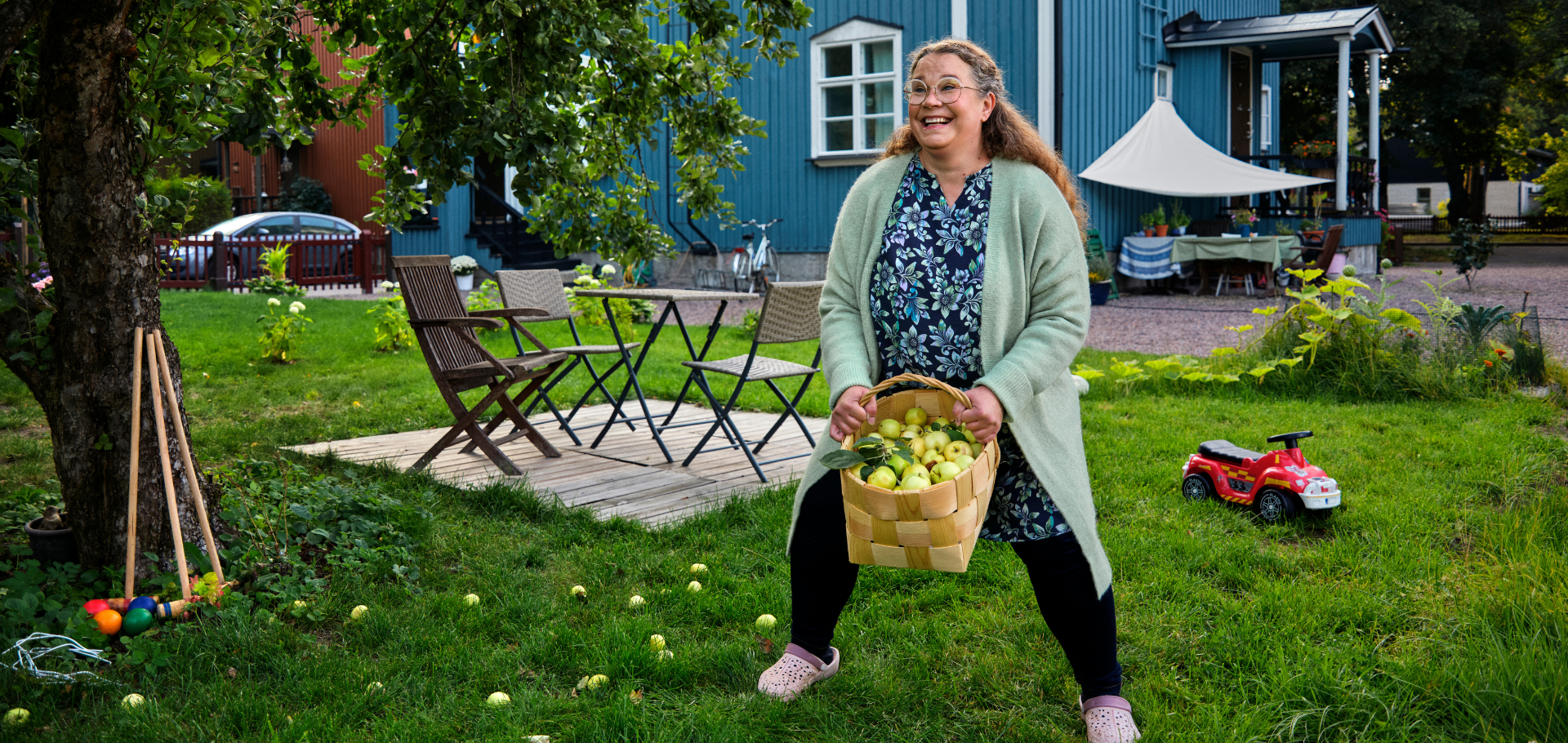 Nainen tekemässä syksyisessä puutarhassa jalkakyykkyä omenakorin kanssa.